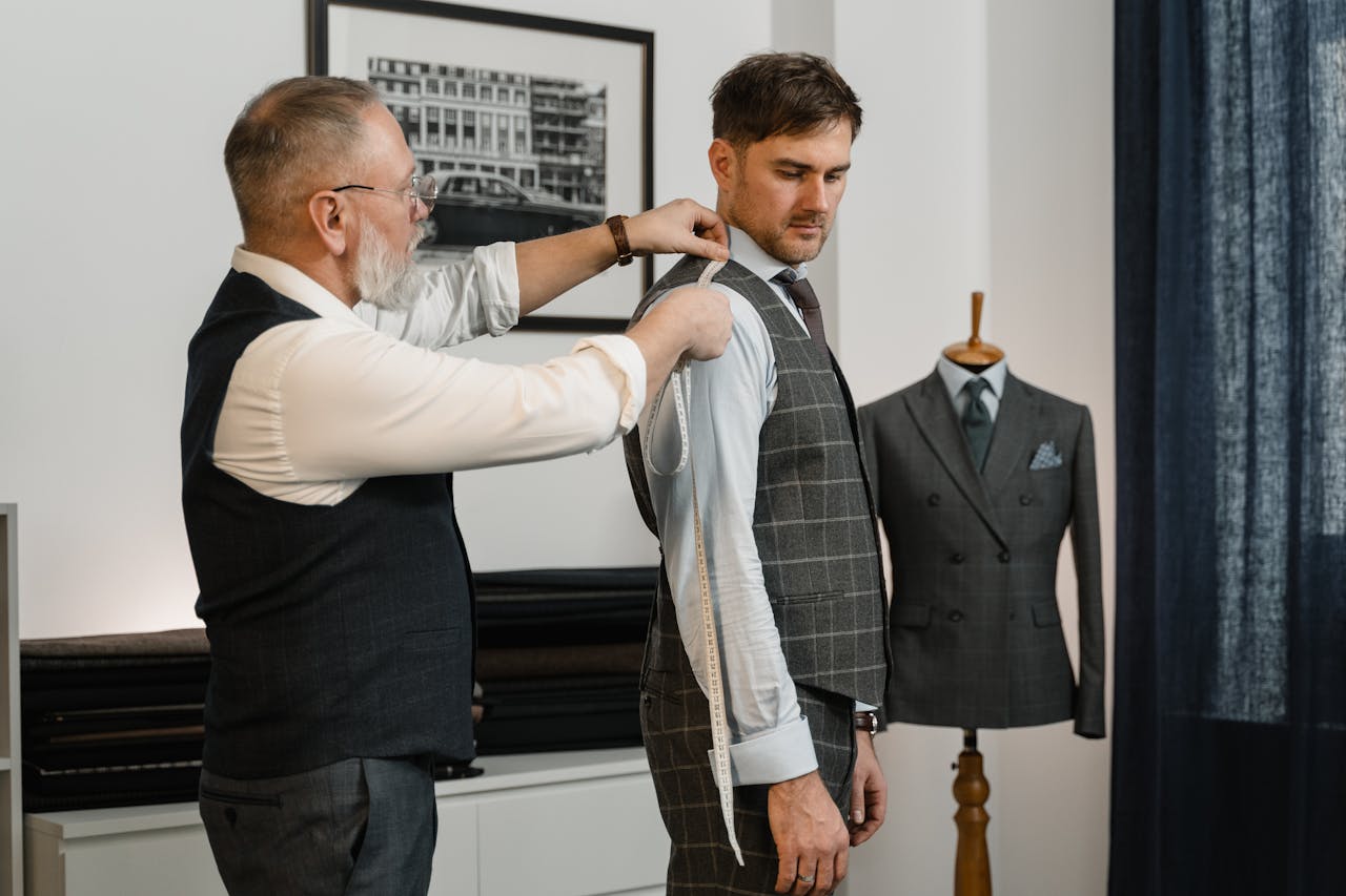 why-choose-us Tailor expertly measuring client for a custom-made suit in a stylish workshop.